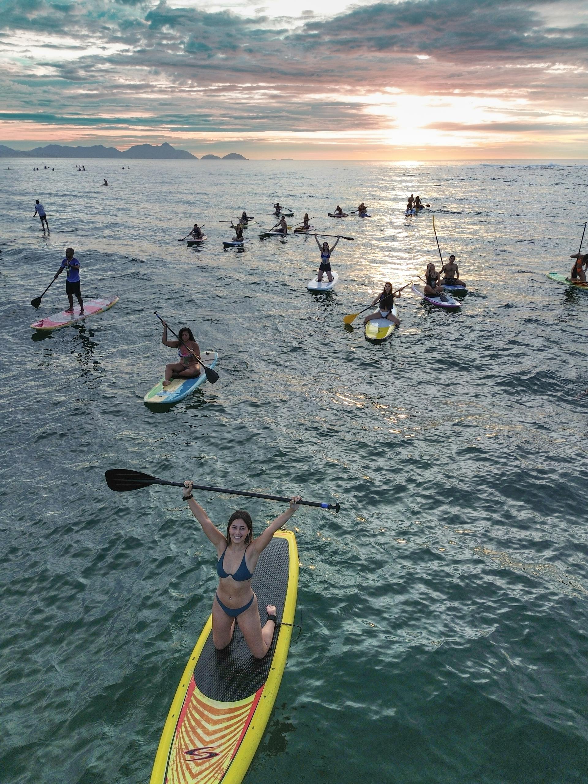A group enjoys paddleboarding in the ocean at sunset, highlighting leisure and water sports.
